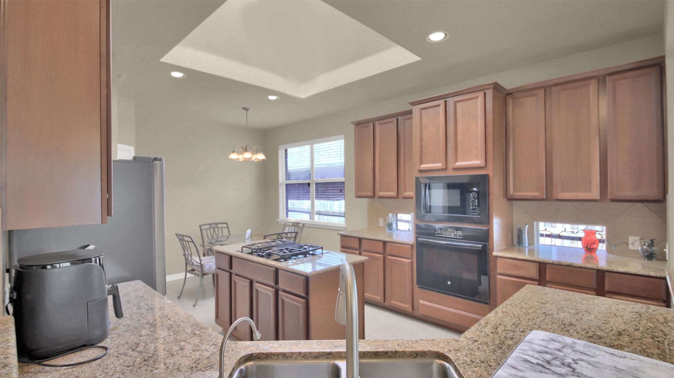 2979 Freemont Street Round Rock, TX 78681 - Photo 17 of 40 Kitchen with wood finish cabinets, black appliances, a tray ceiling, a chandelier, and light stone countertops