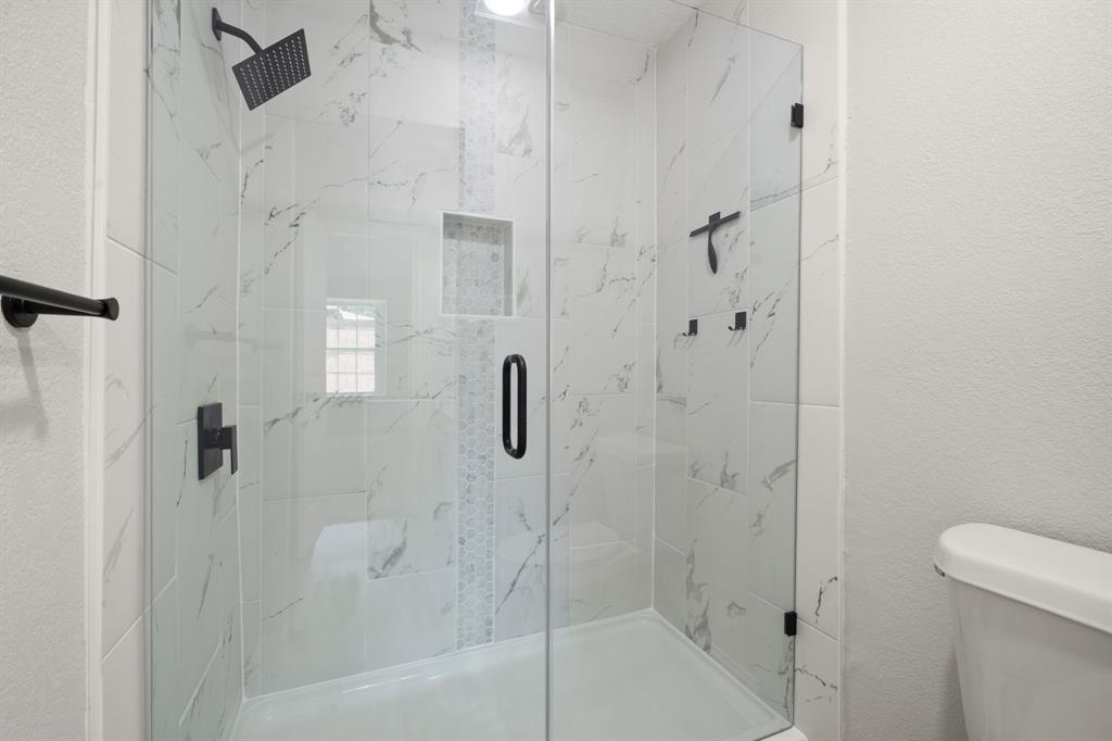 310 Valley Spring Drive Arlington, TX 76018 - Photo 16 of 24 Glass-enclosed shower featuring white marble-look tile, a decorative tile accent strip, and matte black fixtures including a rain showerhead