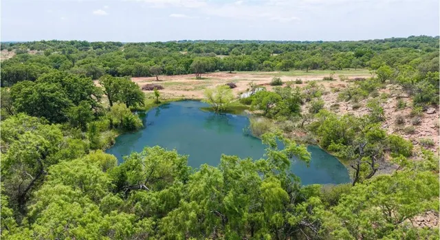 an aerial view of a houses with outdoor space and trees all around