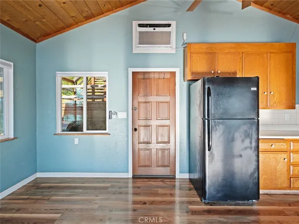 a view of a refrigerator in kitchen and an empty room with wooden floor