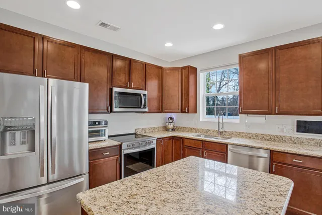 a kitchen with stainless steel appliances granite countertop a sink a stove a refrigerator cabinets and a window