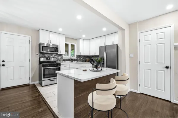 a kitchen with stainless steel appliances kitchen island granite countertop a stove a sink a refrigerator and white cabinets with wooden floor