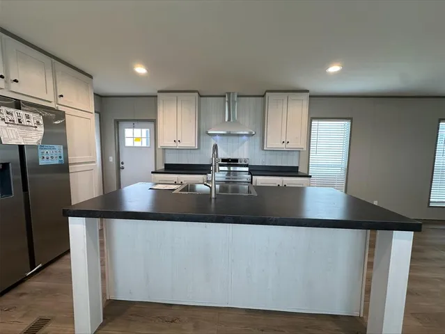 a kitchen with kitchen island granite countertop a sink a refrigerator and white cabinets