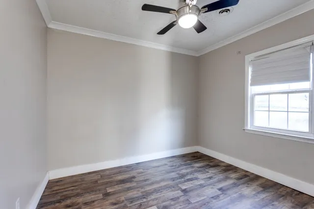 an empty room with wooden floor chandelier fan and windows