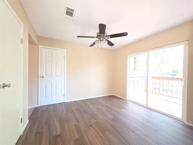 an empty room with wooden floor fan and windows
