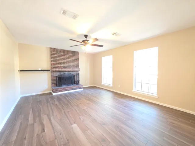an empty room with wooden floor fireplace and windows