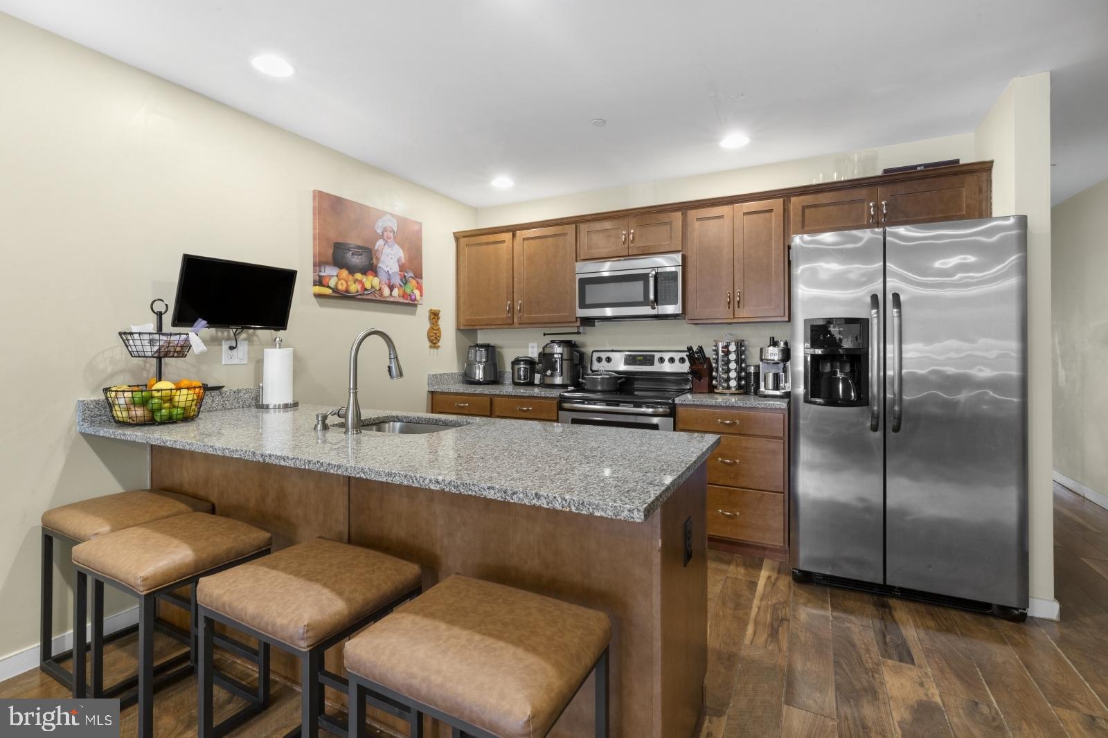 a kitchen with stainless steel appliances granite countertop a refrigerator a sink a stove a microwave a dining table and chairs with wooden floor