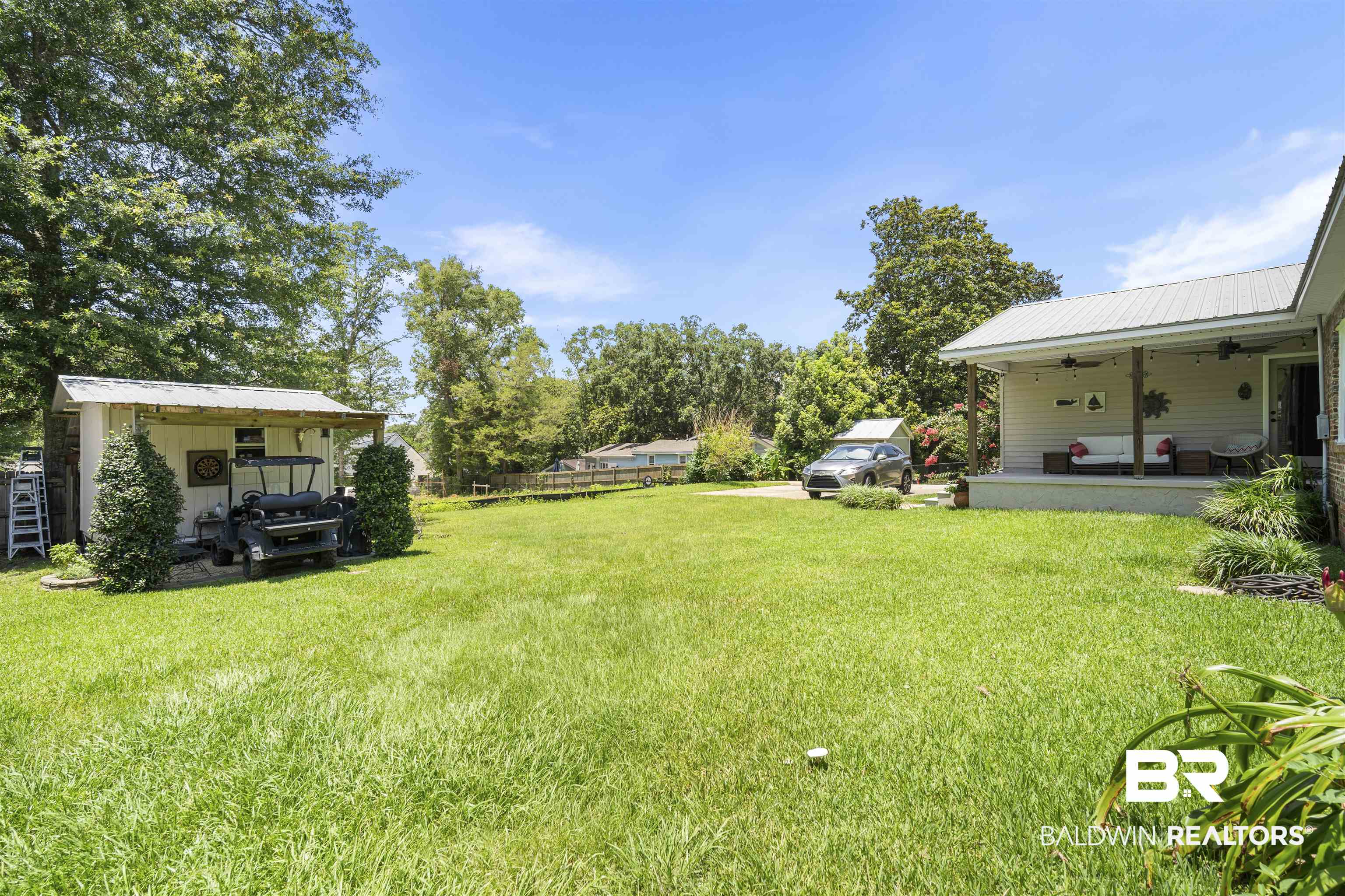 1615 5th Street Daphne, AL 36526 - Photo 25 of 28 Spacious exterior featuring a large grassy area, a covered outdoor living space with a metal roof, a gravel driveway, a detached storage shed, and mature trees