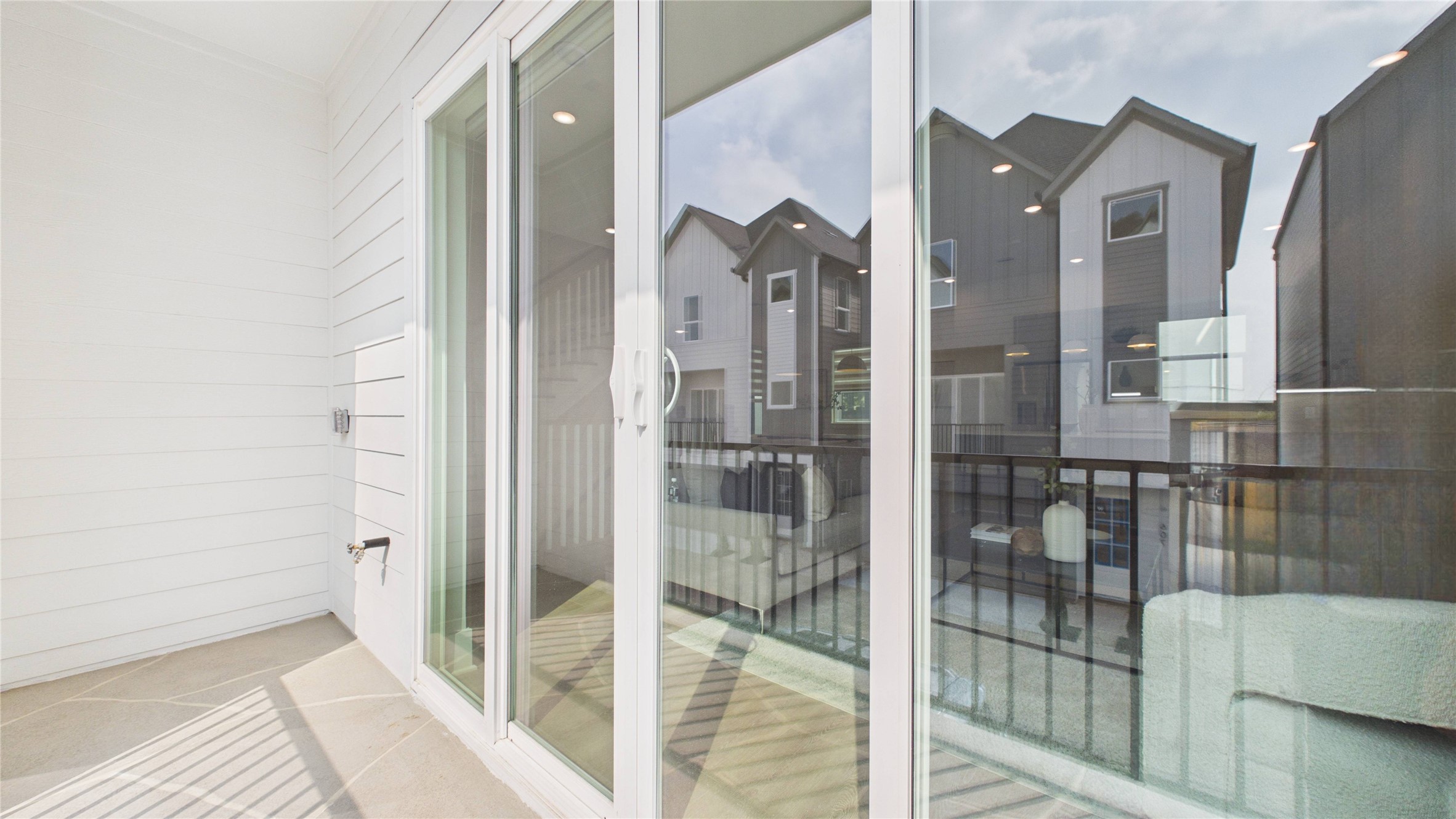 602 Skyland Terrace Way Houston, TX 77009 - Photo 18 of 40 This photo shows a bright, modern balcony with sliding glass doors, providing a view of neighboring houses. The space features clean white siding and a sleek railing, perfect for enjoying outdoor moments.