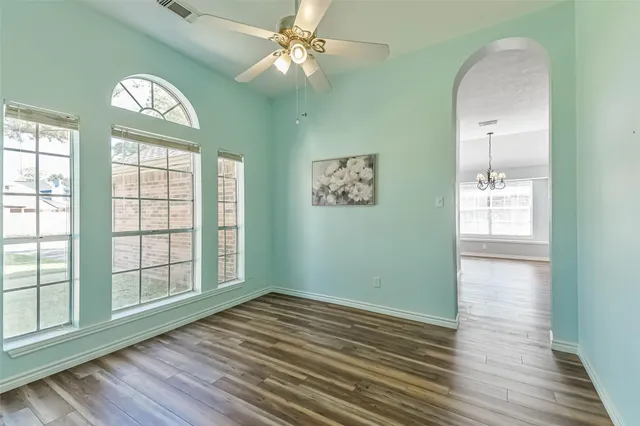 an empty room with wooden floor fan and windows