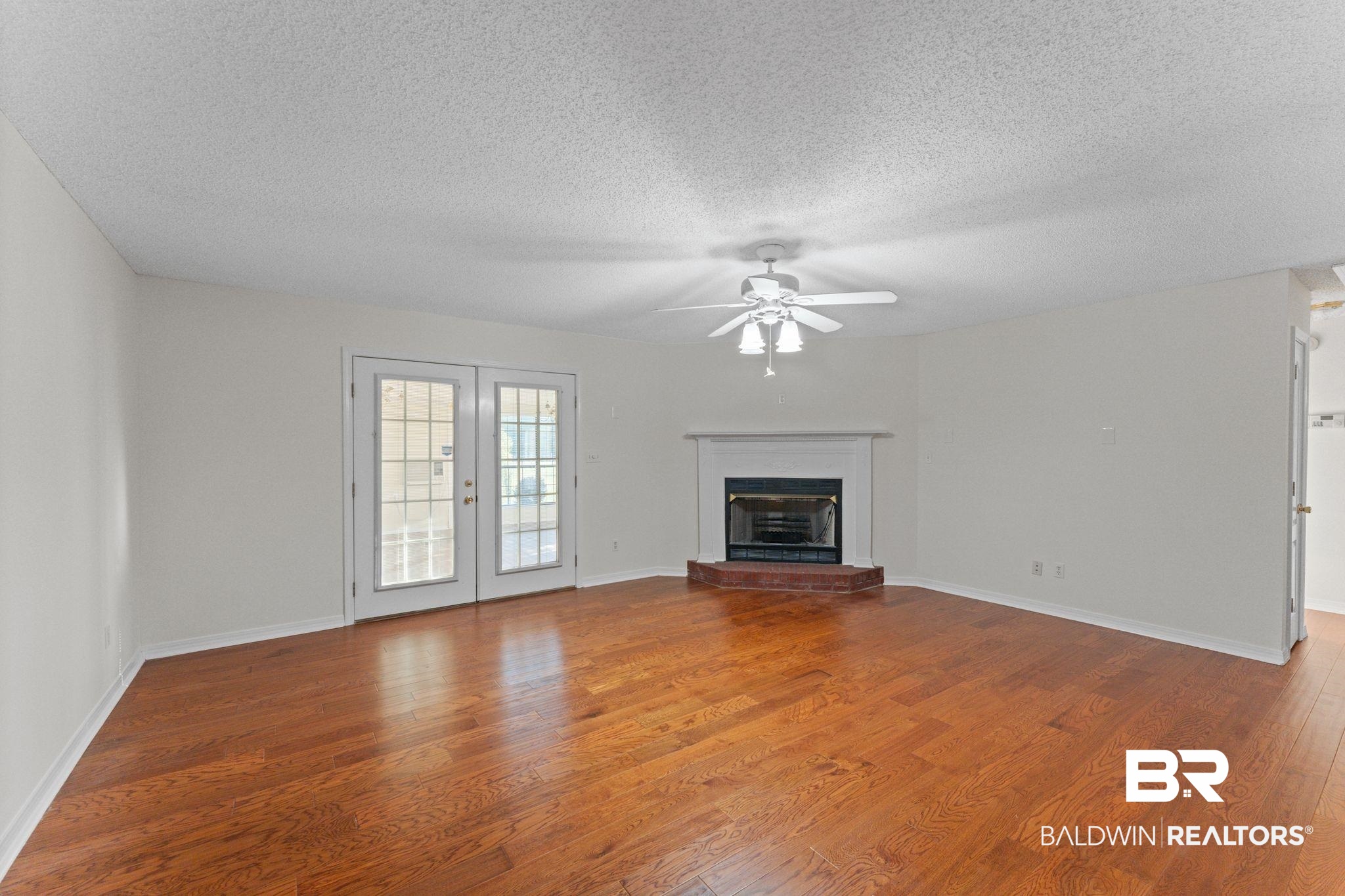 888 Mobile Cut-Off Road St. Stephens, AL 36569 - Photo 19 of 54 Unfurnished living room with wood finished floors, a fireplace with raised hearth, a textured ceiling, a ceiling fan, and french doors