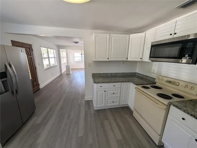 a kitchen with granite countertop a refrigerator a stove a sink and white cabinets with wooden floor