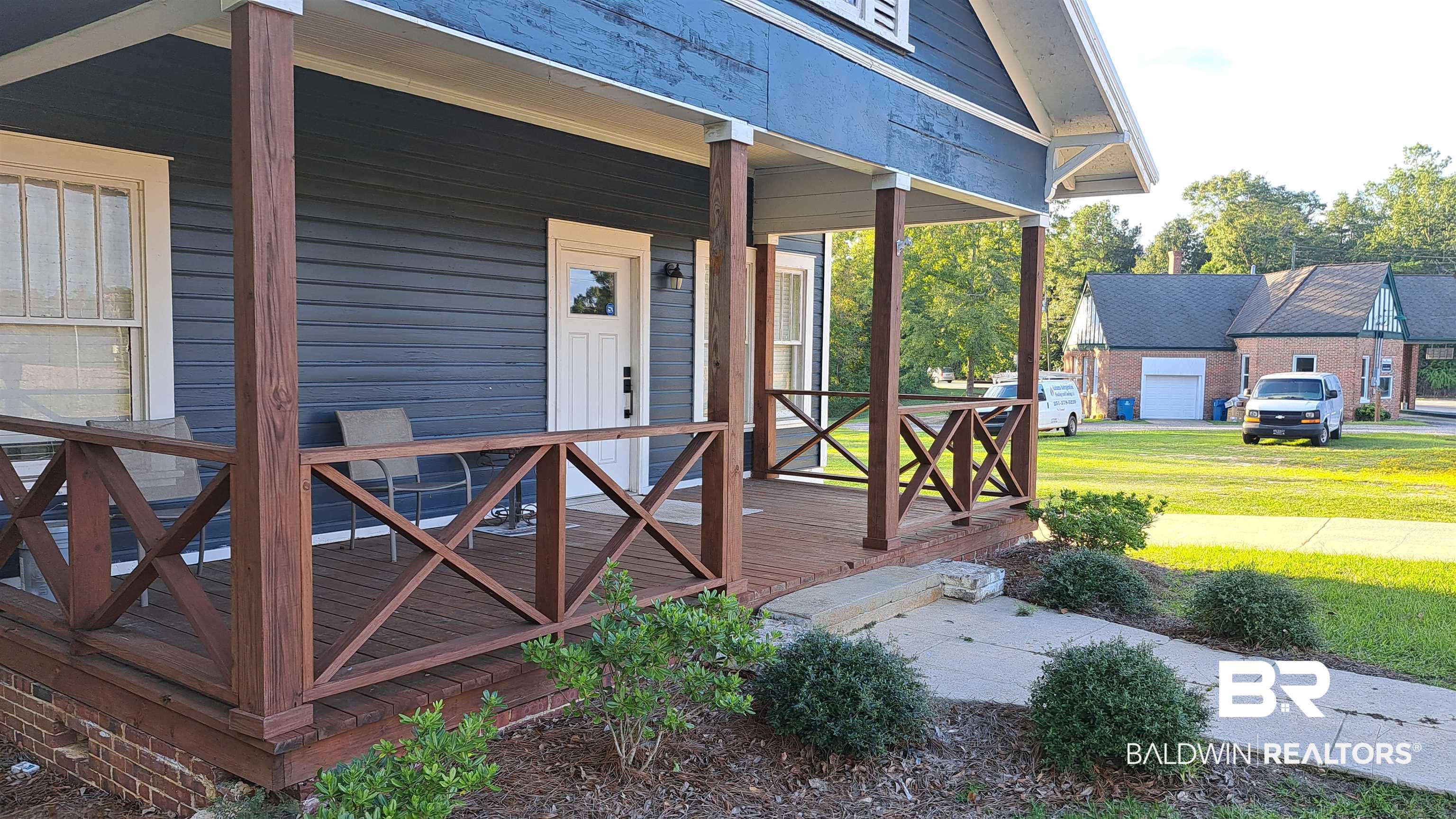 110 South Main Street Evergreen, AL 36401 - Photo 2 of 27 Inviting covered porch with natural wood posts and railings, blue siding, white trim, and a white entry door
