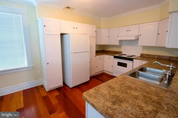 a kitchen with granite countertop a refrigerator a stove a sink and white cabinets with wooden floor