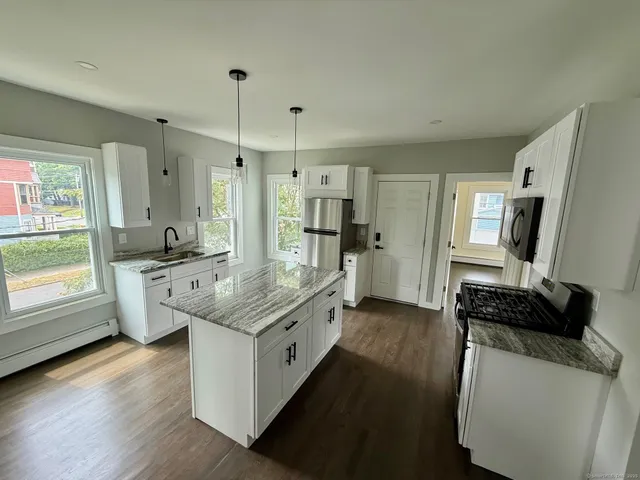 a kitchen with stainless steel appliances granite countertop a stove a sink dishwasher a refrigerator and white cabinets with wooden floor