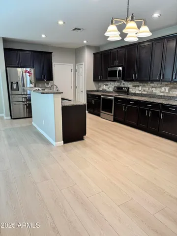 a kitchen with stainless steel appliances kitchen island granite countertop a stove top oven a sink dishwasher and a refrigerator with wooden cabinets