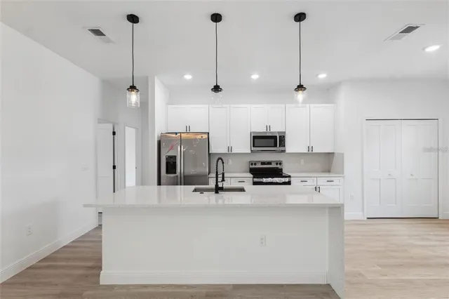 a kitchen with stainless steel appliances kitchen island granite countertop a sink a microwave a refrigerator and white cabinets