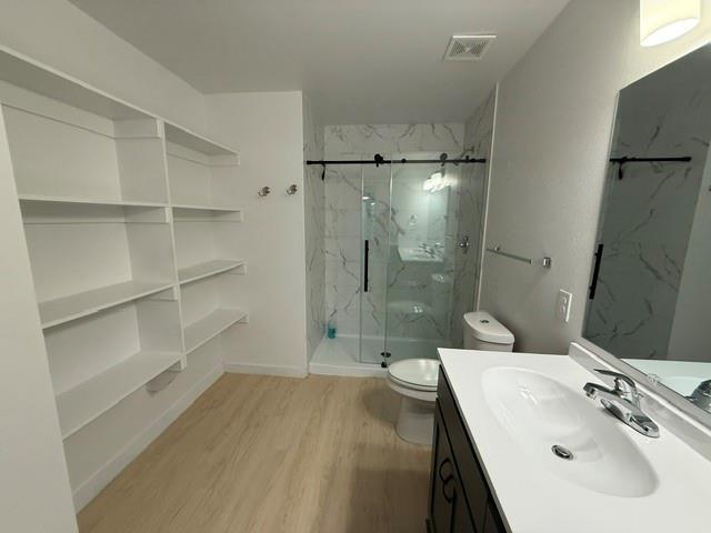 505 Thomas Street Terrell, TX 75160 - Photo 23 of 38 Bathroom featuring a built-in shelving unit, glass-enclosed shower with tile surround, a vanity with an integrated sink, and light wood-finish flooring