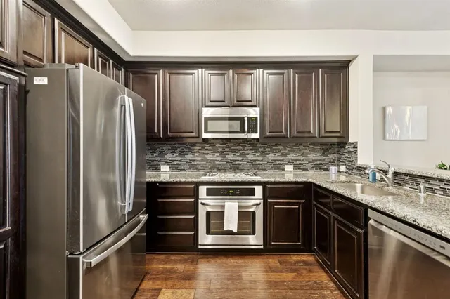 a kitchen with stainless steel appliances granite countertop a refrigerator a stove a sink a dining table and chairs with wooden floor