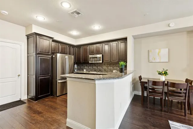 a kitchen with stainless steel appliances kitchen island granite countertop a table chairs and a refrigerator