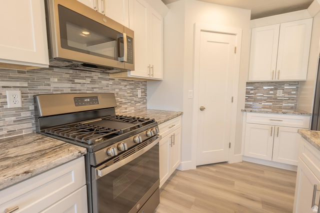 910 East Remington Road Cedar City, UT 84721 - Photo 5 of 29 Kitchen featuring stainless steel appliances, white cabinetry, a tiled backsplash, wood-finish flooring, and light-toned countertops