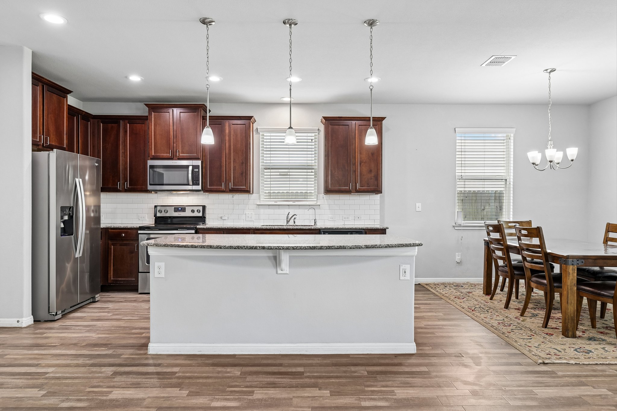 387 Guemal Road Buda, TX 78610 - Photo 10 of 39 Kitchen featuring a central island with granite countertop, stainless steel appliances, dark wood cabinetry, subway tile backsplash, and wood-finish flooring