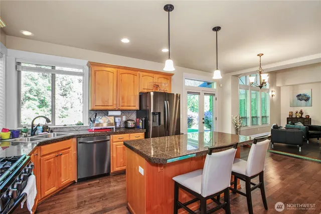 a kitchen with stainless steel appliances granite countertop a stove top oven a sink dishwasher a dining table and chairs with wooden floor