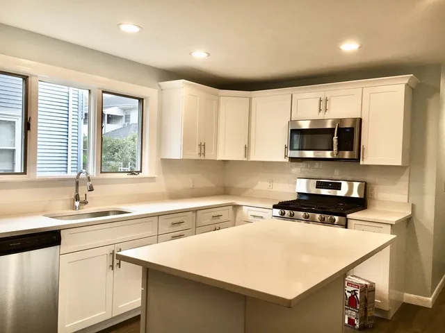 a kitchen with stainless steel appliances a sink a stove a microwave and white cabinets
