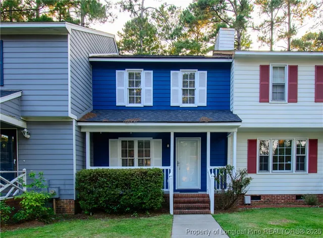 a view of brick house with a small yard plants and a large tree
