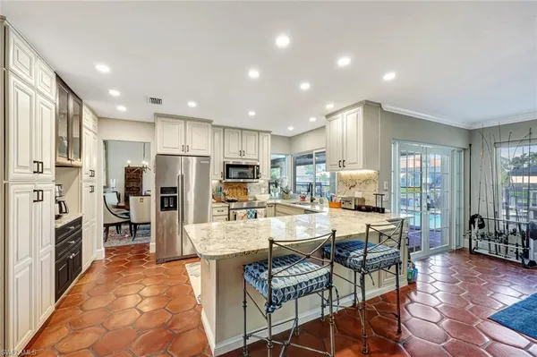 a kitchen with stainless steel appliances kitchen island granite countertop a refrigerator oven a sink a dining table and chairs with wooden floor