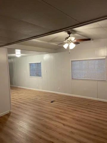 a view of an empty room with wooden floor and fan