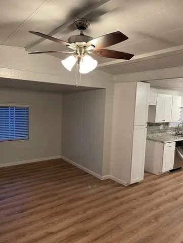 an empty room with wooden floor a ceiling fan and kitchen view