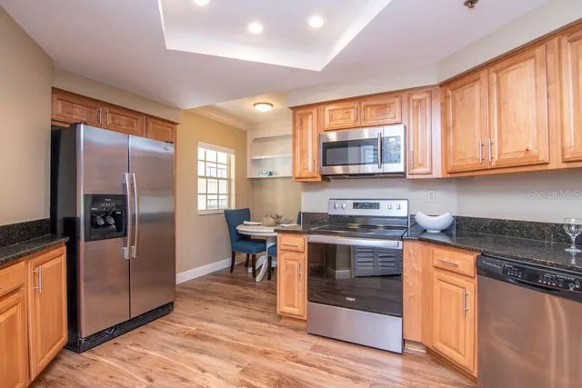 a kitchen with stainless steel appliances granite countertop wooden cabinets a sink a stove a dining table and chairs