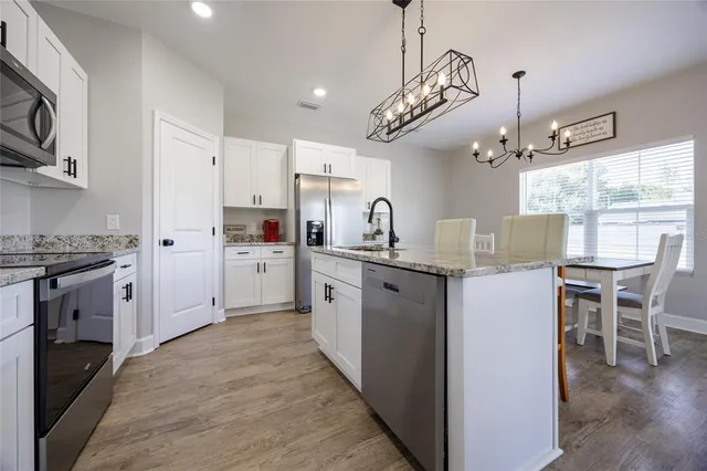 a kitchen with stainless steel appliances a refrigerator a stove a sink dishwasher a dining table and chairs with wooden floor