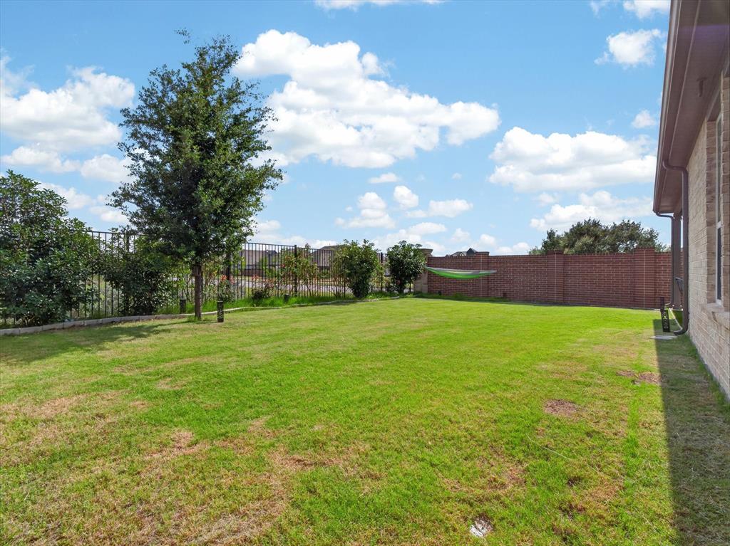 636 Corner Post Path Celina, TX 75009 - Photo 35 of 40 Expansive grass lawn featuring a perimeter brick wall, black metal fencing, and mature trees