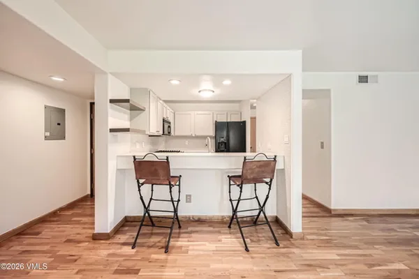a white kitchen with stainless steel appliances kitchen island granite countertop a dining table chairs and a refrigerator