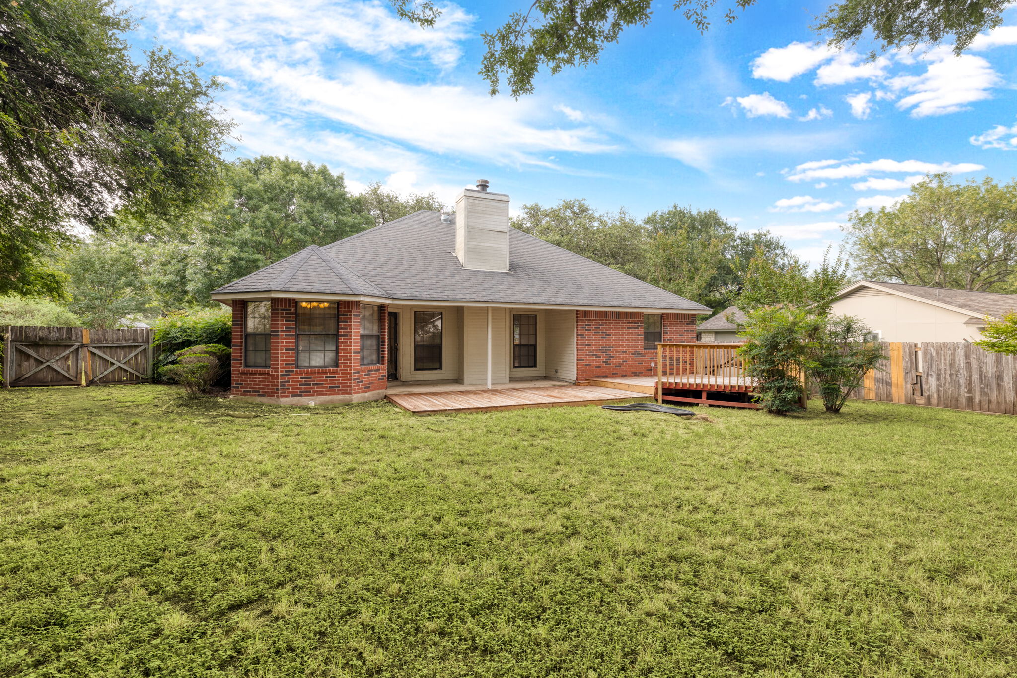 1502 Oak Knoll Lane Lockhart, TX 78644 - Photo 17 of 18 Rear view of house with a fenced backyard, a wooden deck, a chimney, a gate, and brick siding