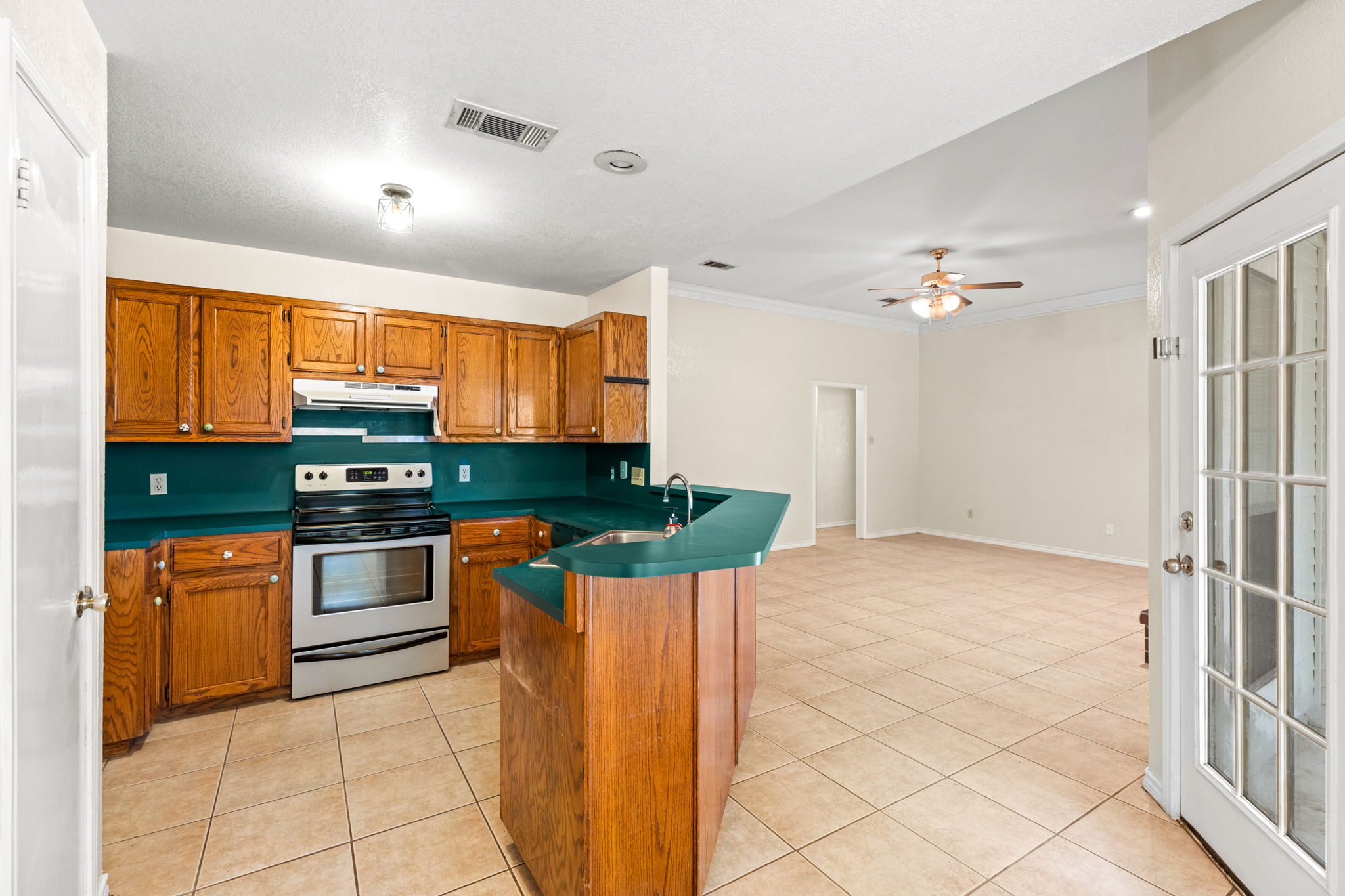 1502 Oak Knoll Lane Lockhart, TX 78644 - Photo 7 of 18 Kitchen with stainless steel electric range oven, brown cabinetry, ceiling fan, light tile patterned floors.