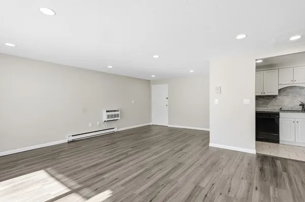 a view of empty room with wooden floor and kitchen