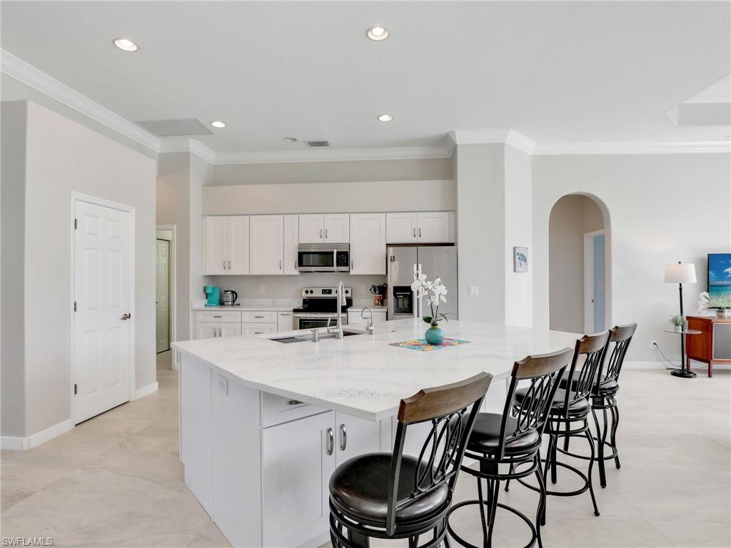 8845 Lely Island Circle Naples, FL 34113 - Photo 17 of 45 a kitchen with stainless steel appliances a dining table chairs and white cabinets