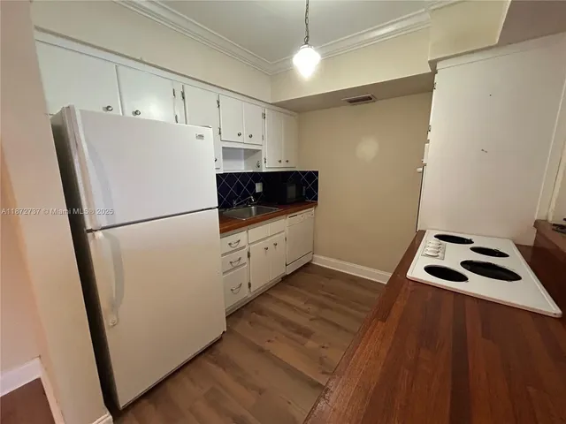 a kitchen with granite countertop a refrigerator a sink and white cabinets
