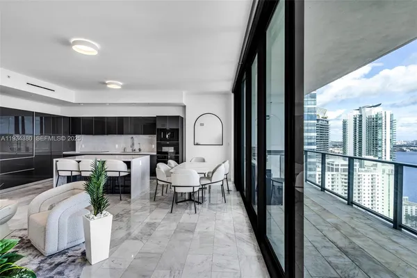 a living room with chairs a rug kitchen view and a large window