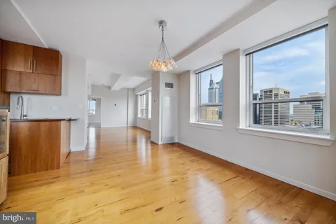 a view of an empty room with window and kitchen view