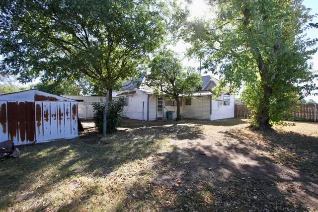 a view of a backyard with large trees and wooden fence