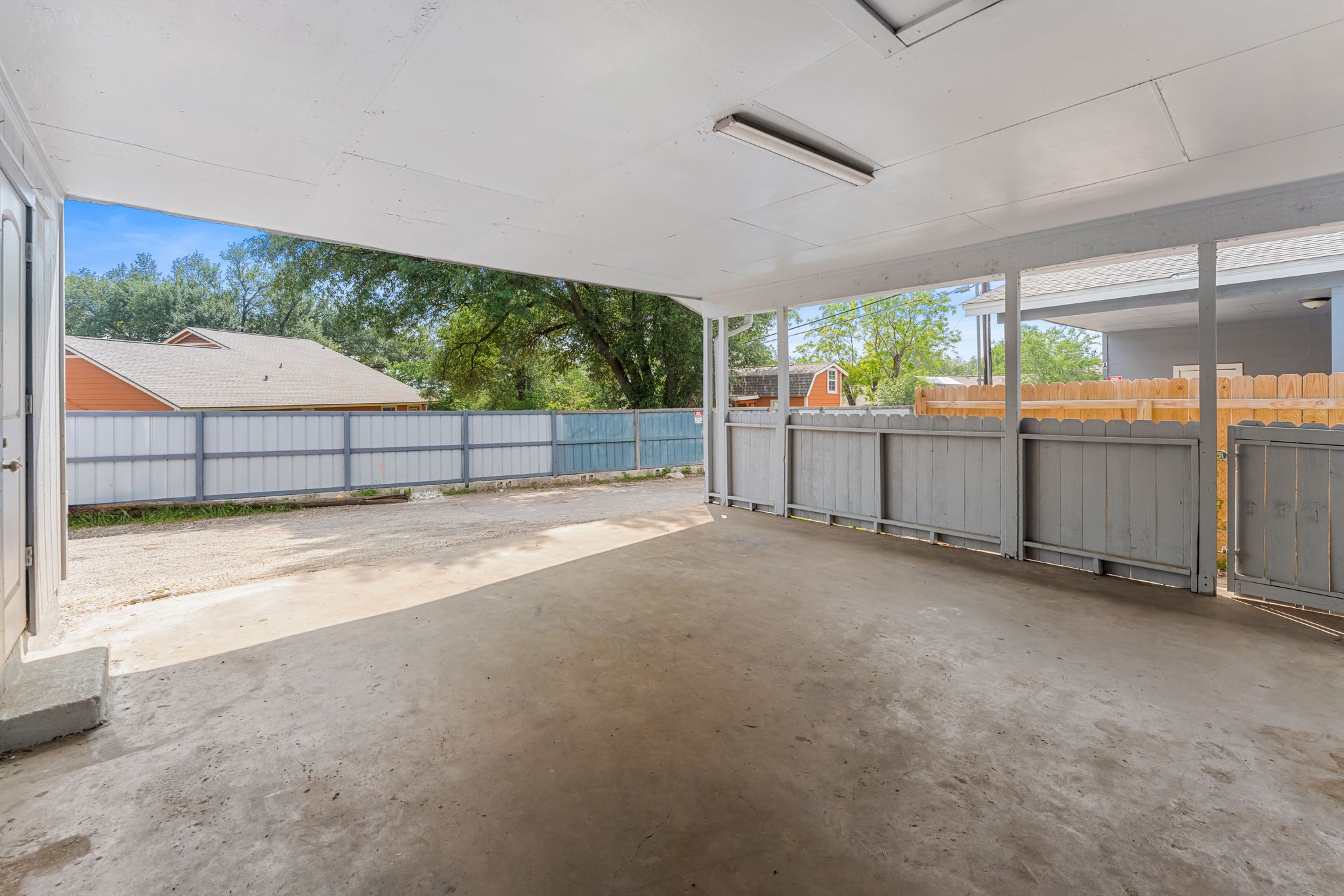 2501 Teri Road, Unit B Austin, TX 78744 - Photo 20 of 21 Covered patio featuring a concrete slab floor, exposed white ceiling beams, fluorescent lighting, and partial privacy fencing
