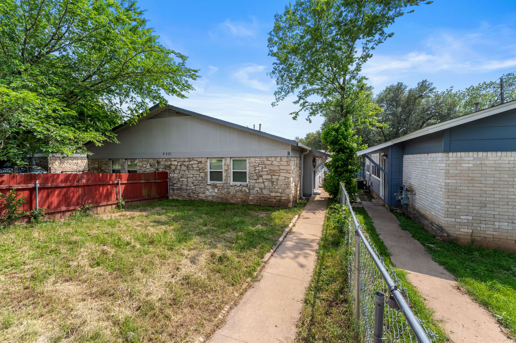 2501 Teri Road, Unit B Austin, TX 78744 - Photo 21 of 21 Stone veneer facade property featuring a red painted wood fence, established trees, and a concrete pathway