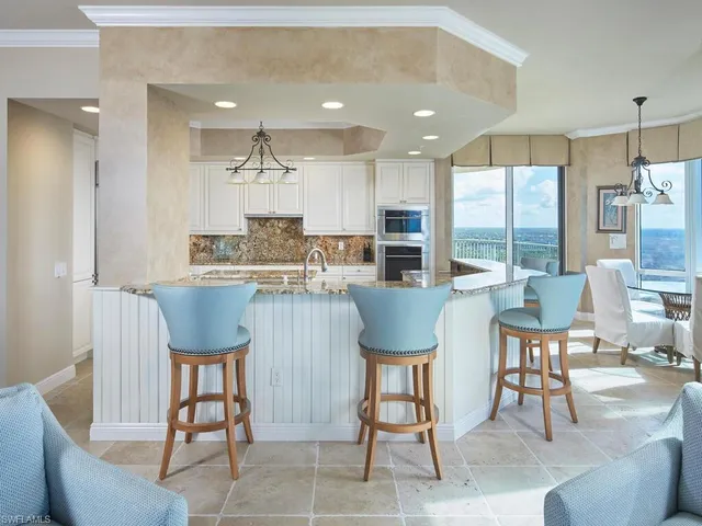 a dining hall with stainless steel appliances kitchen island granite countertop a dining table chairs and a refrigerator