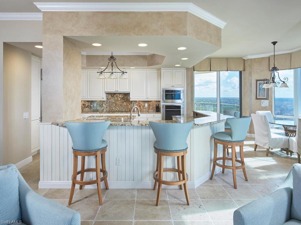 23750 Via Trevi Way, Unit 2001 Estero, FL 34134 - Photo 12 of 26 Kitchen with a chandelier, crown molding, light stone countertops, white cabinetry, and backsplash