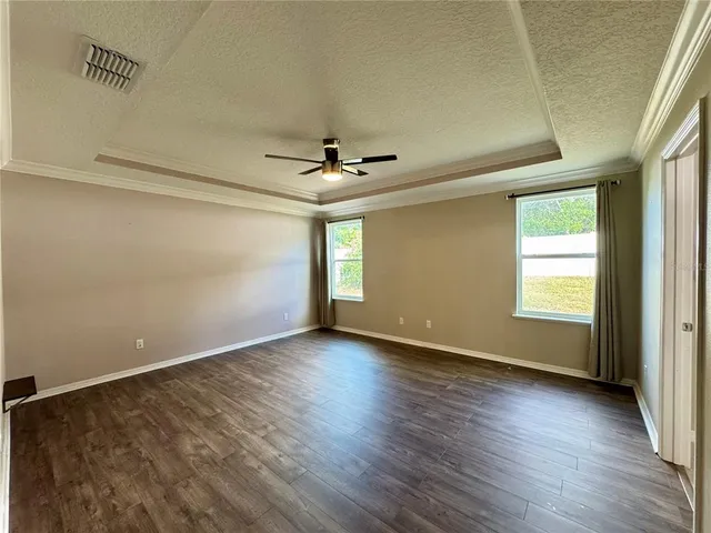 an empty room with wooden floor a ceiling fan and windows
