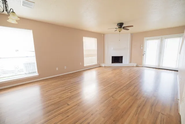 an empty room with wooden floor ceiling fan and windows